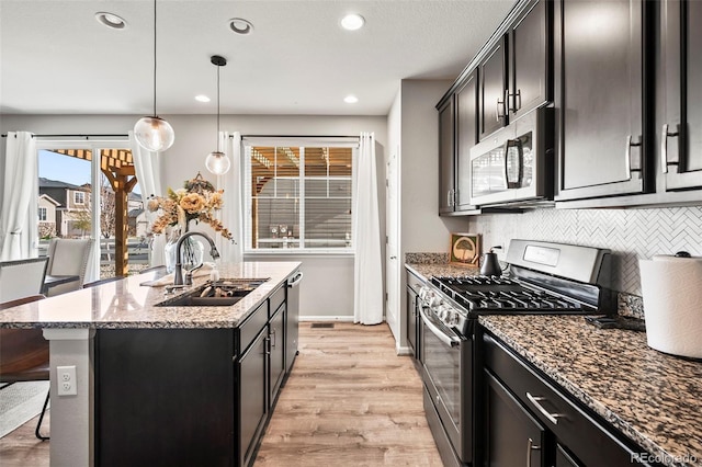 kitchen featuring sink, an island with sink, light hardwood / wood-style floors, pendant lighting, and appliances with stainless steel finishes