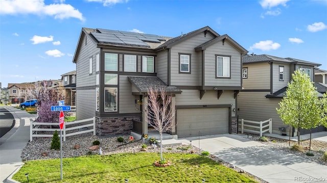 view of front of property with driveway, stone siding, fence, an attached garage, and solar panels