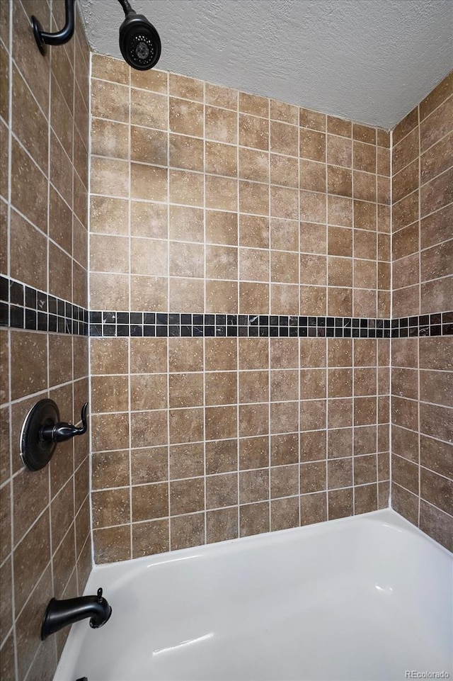 bathroom with a textured ceiling and tiled shower / bath combo