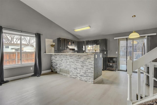 kitchen featuring decorative backsplash, light wood-type flooring, kitchen peninsula, and vaulted ceiling