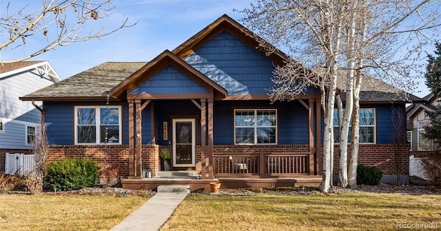 bungalow-style house with a front yard, covered porch, brick siding, and roof with shingles