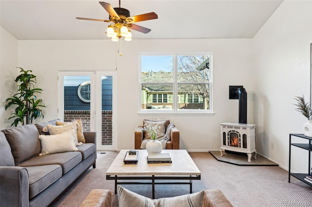 living area with light colored carpet, baseboards, a wood stove, and ceiling fan