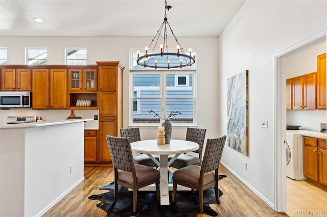 dining room featuring a notable chandelier, washer / clothes dryer, baseboards, and light wood finished floors