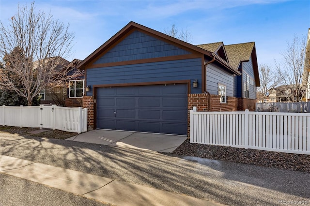 view of property exterior with driveway, a garage, brick siding, and a fenced front yard