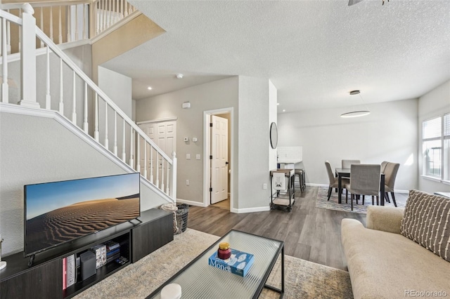 living room with a textured ceiling, stairway, wood finished floors, and baseboards