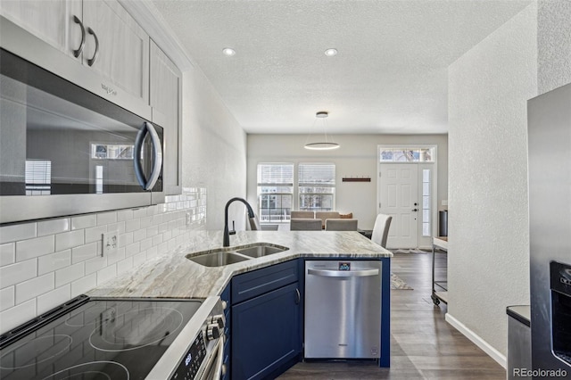 kitchen with a textured wall, appliances with stainless steel finishes, a sink, blue cabinets, and a peninsula