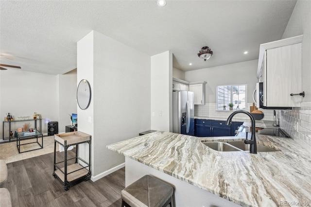 kitchen featuring blue cabinets, stainless steel appliances, a peninsula, a sink, and dark wood finished floors