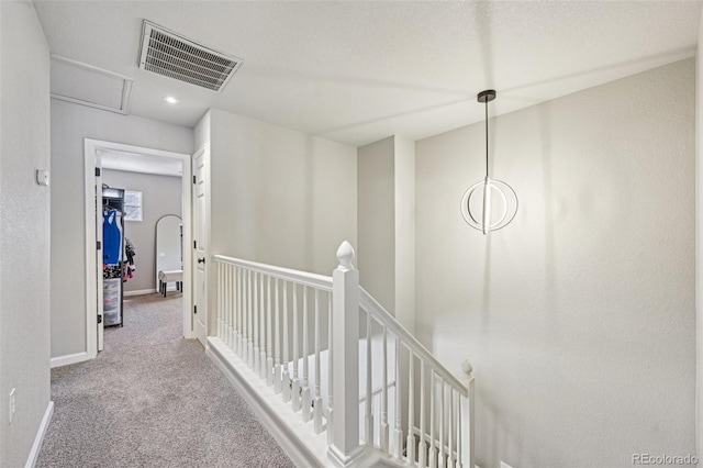 hall with carpet floors, an upstairs landing, visible vents, and baseboards