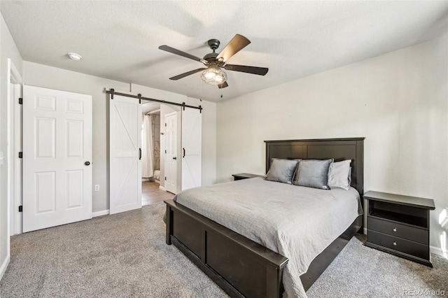 carpeted bedroom with a barn door, baseboards, ensuite bath, ceiling fan, and a textured ceiling