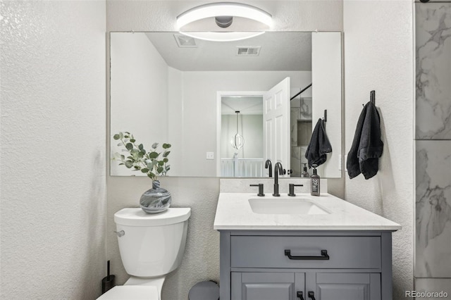 bathroom with visible vents, a textured wall, vanity, and toilet