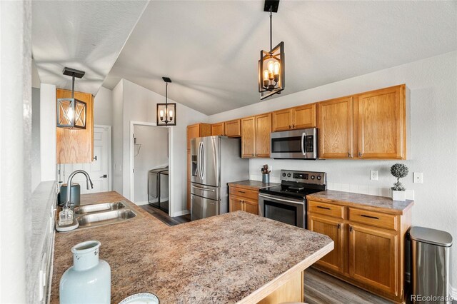 8617 W 17th Street Dr, Greeley, CO 80634 - kitchen featuring appliances with stainless steel finishes, washing machine and clothes dryer, a sink, wood finished floors, and vaulted ceiling