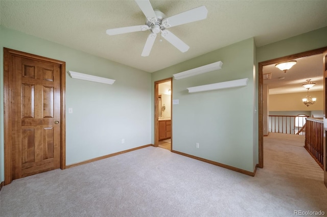 unfurnished bedroom featuring a textured ceiling, ensuite bathroom, light carpet, and ceiling fan with notable chandelier