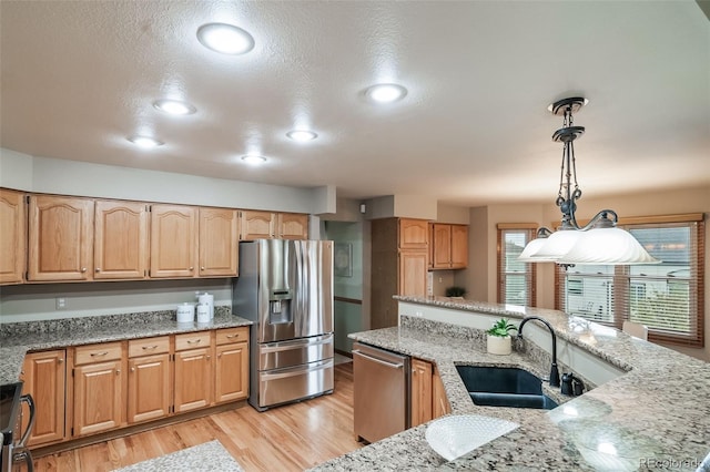 kitchen featuring sink, stainless steel appliances, light stone counters, light hardwood / wood-style flooring, and decorative light fixtures