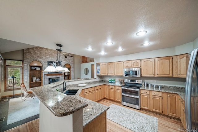 kitchen with sink, appliances with stainless steel finishes, decorative light fixtures, light hardwood / wood-style floors, and kitchen peninsula