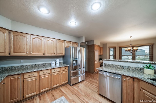 kitchen with appliances with stainless steel finishes, stone countertops, light hardwood / wood-style flooring, decorative light fixtures, and a notable chandelier