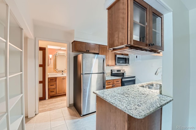 kitchen with light tile patterned floors, sink, kitchen peninsula, stainless steel appliances, and light stone countertops