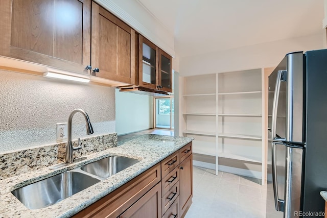 kitchen with light tile patterned floors, light stone countertops, stainless steel fridge, and sink