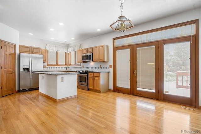 kitchen with a notable chandelier, appliances with stainless steel finishes, french doors, light wood-style flooring, and a kitchen island
