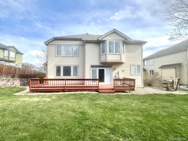 back of property with a shingled roof, fence, a wooden deck, and a lawn