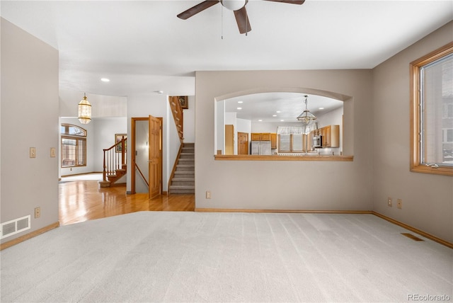 unfurnished living room with carpet, visible vents, ceiling fan, and stairway
