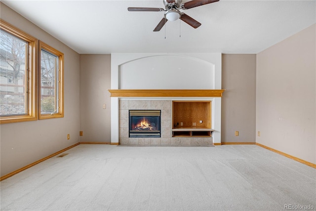 unfurnished living room with carpet, ceiling fan, a tiled fireplace, baseboards, and visible vents