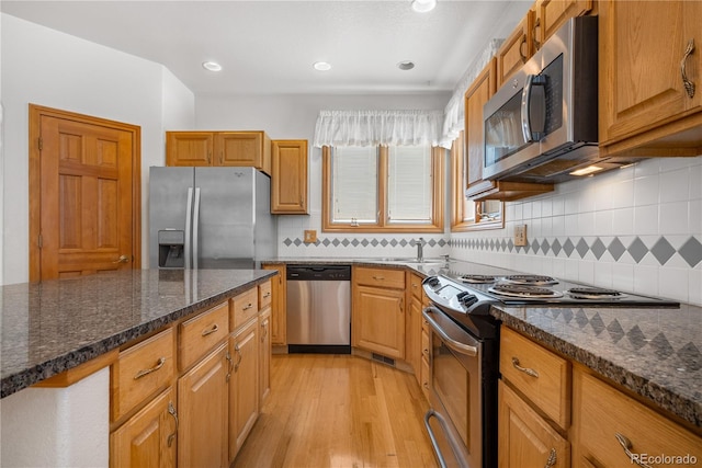 kitchen featuring dark stone counters, light wood-type flooring, recessed lighting, appliances with stainless steel finishes, and decorative backsplash