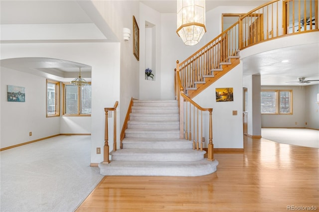 stairway featuring arched walkways, baseboards, ceiling fan with notable chandelier, and wood finished floors