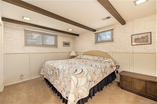 carpeted bedroom with visible vents, a decorative wall, beam ceiling, and wainscoting