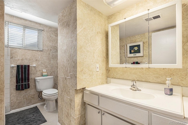 bathroom featuring toilet, vanity, visible vents, and tile walls