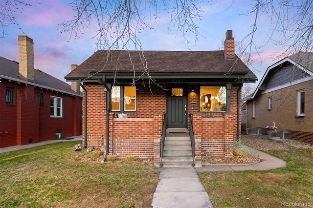 bungalow-style house featuring a lawn, brick siding, roof with shingles, and a chimney