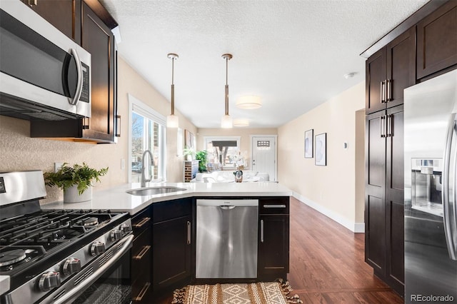 kitchen featuring dark wood-style floors, a peninsula, a sink, stainless steel appliances, and light countertops