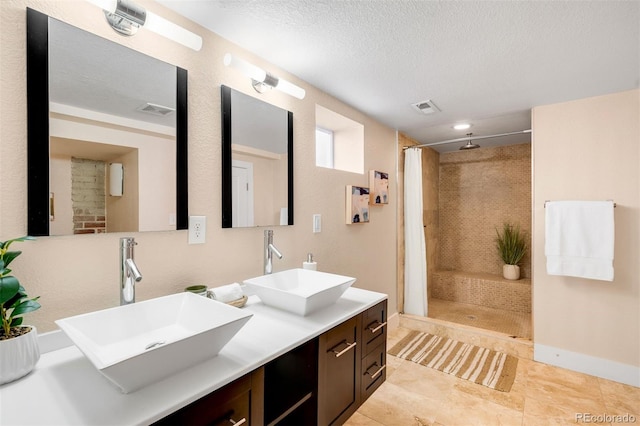 bathroom featuring a sink, visible vents, a textured ceiling, and a tile shower