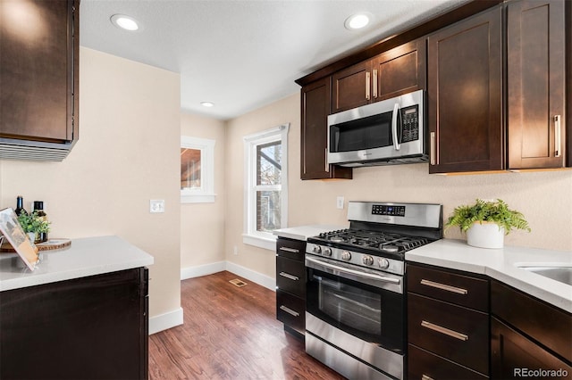 kitchen featuring stainless steel appliances, dark brown cabinetry, light countertops, baseboards, and dark wood-style flooring