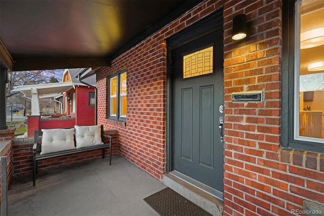 doorway to property featuring a porch and brick siding