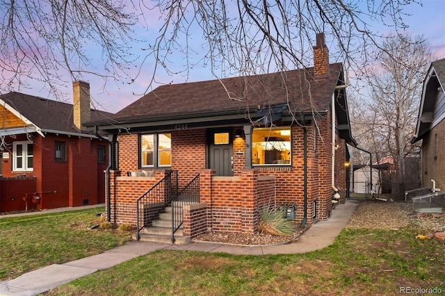 bungalow-style house with a yard, brick siding, a porch, and a chimney