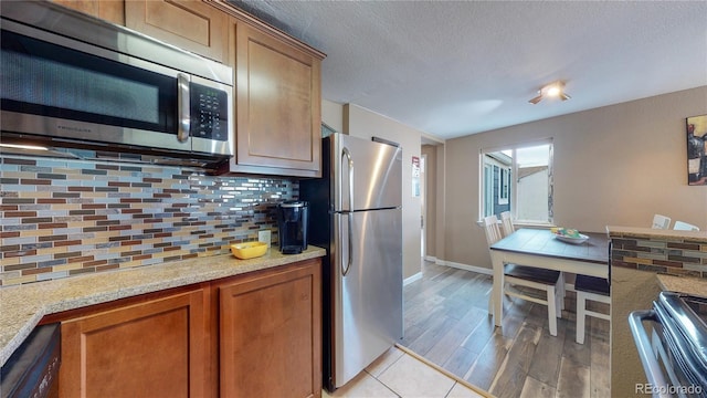 kitchen featuring stainless steel appliances, light stone counters, a textured ceiling, and decorative backsplash