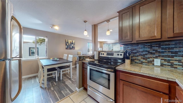 kitchen featuring appliances with stainless steel finishes, pendant lighting, tasteful backsplash, light wood-type flooring, and a textured ceiling