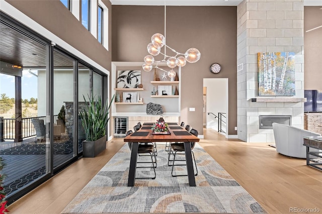 dining area featuring a fireplace, a towering ceiling, wood-type flooring, and a notable chandelier