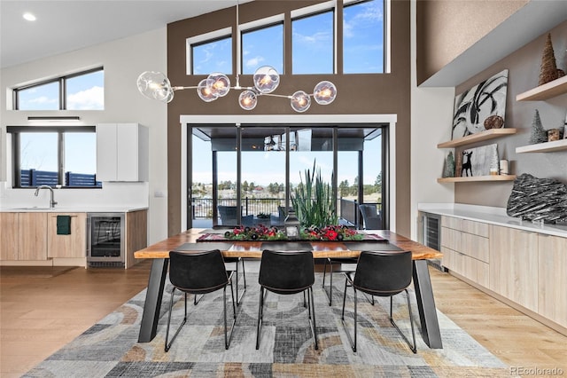 dining space with a towering ceiling, light hardwood / wood-style flooring, beverage cooler, and sink