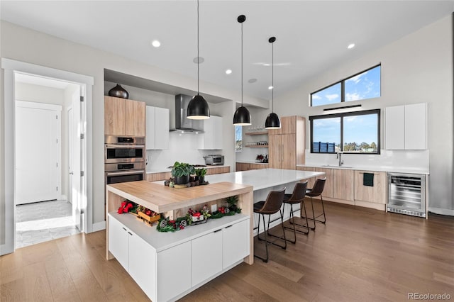 kitchen featuring white cabinets, wall chimney exhaust hood, a kitchen island, and wine cooler