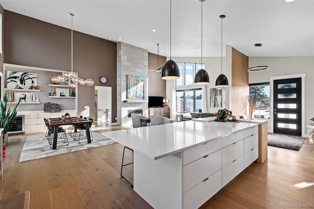 kitchen featuring a large island, a large fireplace, light hardwood / wood-style flooring, pendant lighting, and white cabinets