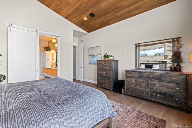 bedroom with connected bathroom, wooden ceiling, a barn door, dark hardwood / wood-style floors, and vaulted ceiling