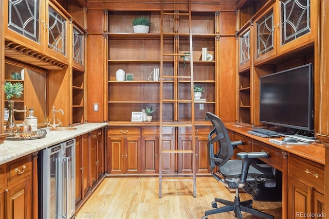 office area with beverage cooler, indoor wet bar, built in desk, a sink, and light wood-style flooring
