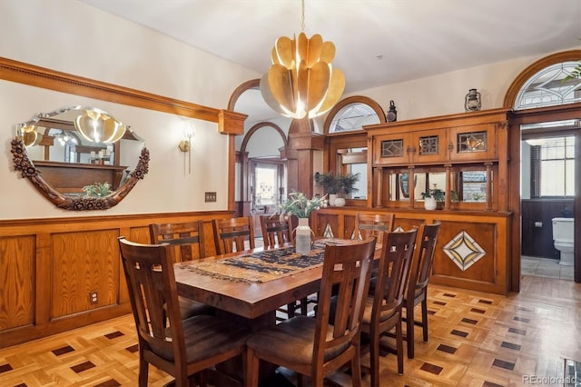 dining area featuring arched walkways, a notable chandelier, and wainscoting
