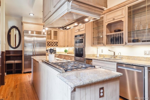 kitchen featuring appliances with stainless steel finishes, range hood, a center island, a sink, and light wood-style floors
