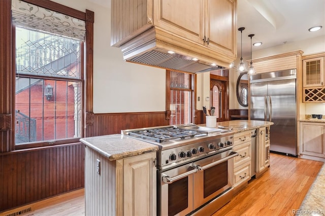 kitchen with a wainscoted wall, high end appliances, light wood-type flooring, visible vents, and glass insert cabinets