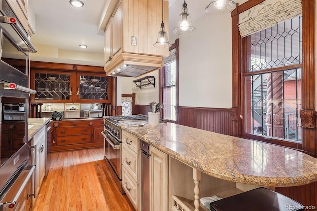 kitchen featuring a wainscoted wall, high end stainless steel range, light stone countertops, and light wood-type flooring