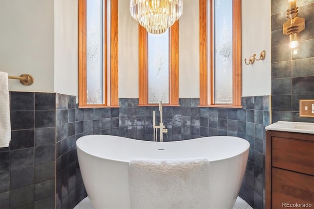 full bathroom with tile walls, a soaking tub, vanity, and a chandelier