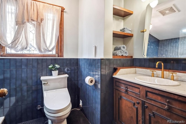 bathroom featuring visible vents, vanity, wainscoting, toilet, and tile walls