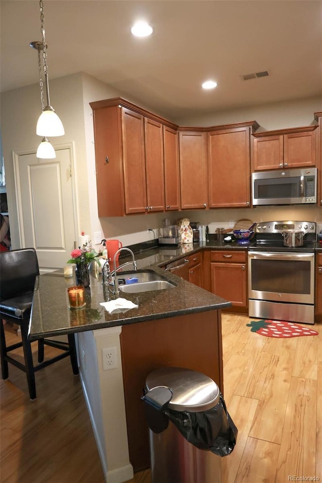 kitchen with a sink, dark stone countertops, stainless steel appliances, a peninsula, and light wood finished floors
